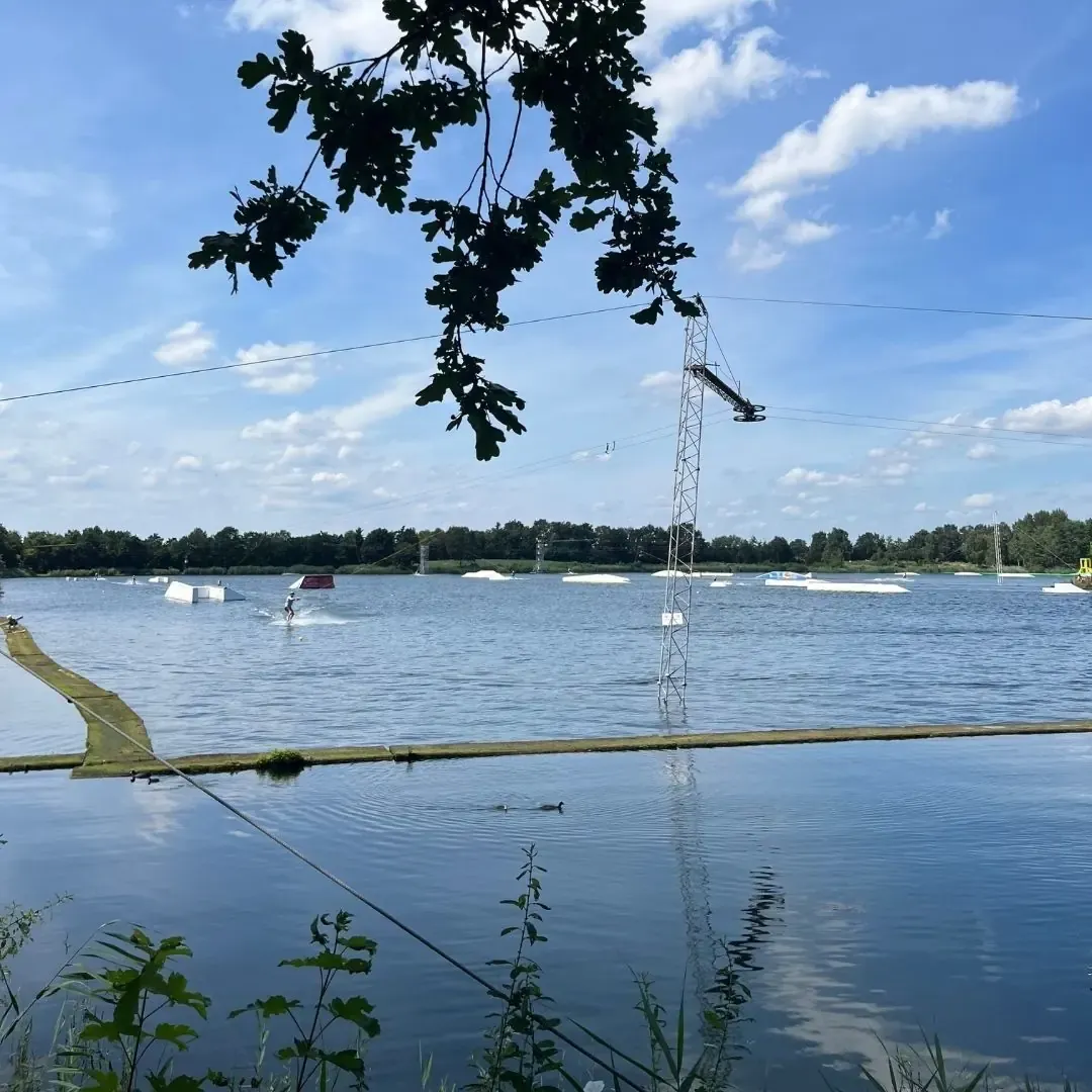Blick durch Eichenzweige auf die Cable-Anlage von Wasserski Alfsee in Rieste
