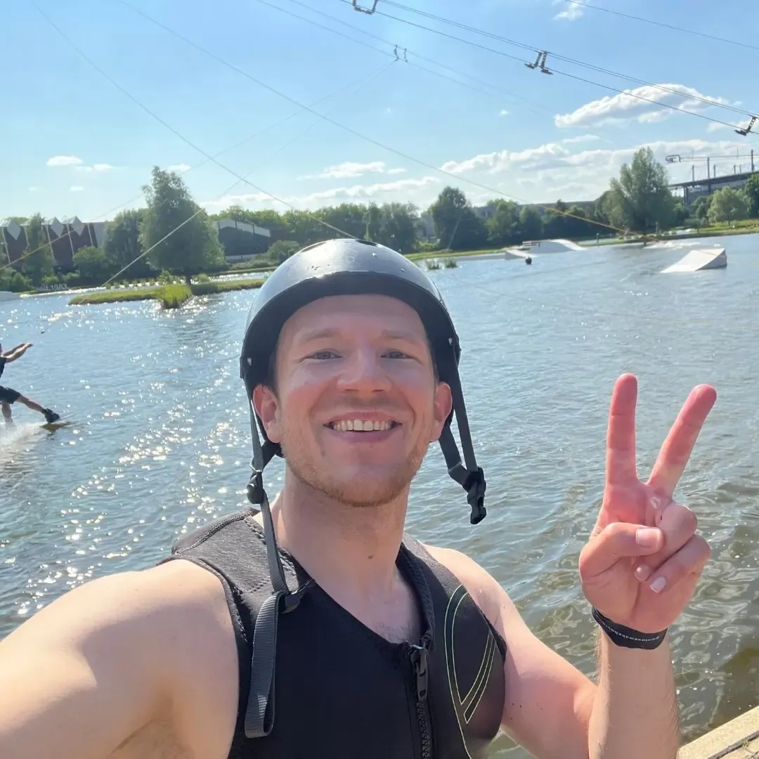 Tobias Schmitz mit Wakeboard-Helm und Peace-Zeichen vor der Cable-Anlage im Wakepark The Bricks in Duisburg