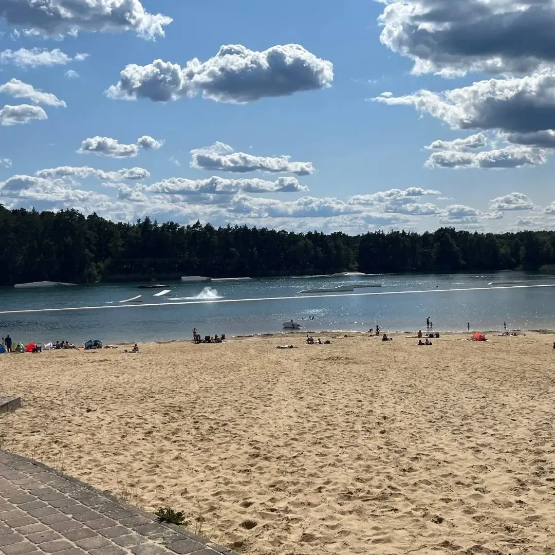 Sandstrand mit Badegästen und Blick auf die Bahn am Wasserski Bernsteinsee