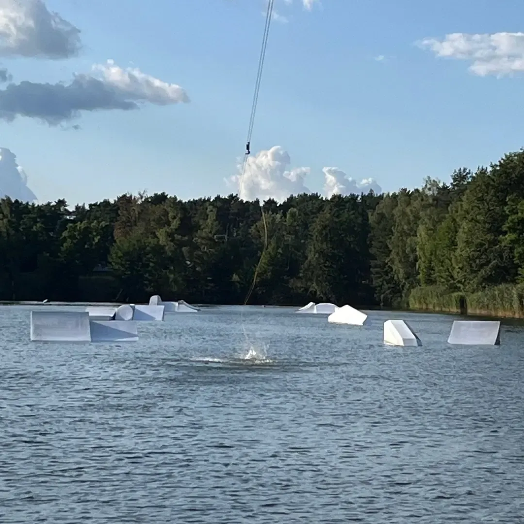 Obstacles im Wasser vor Kiefernwald im Wakepark Wake & Camp Ruhlsdorf